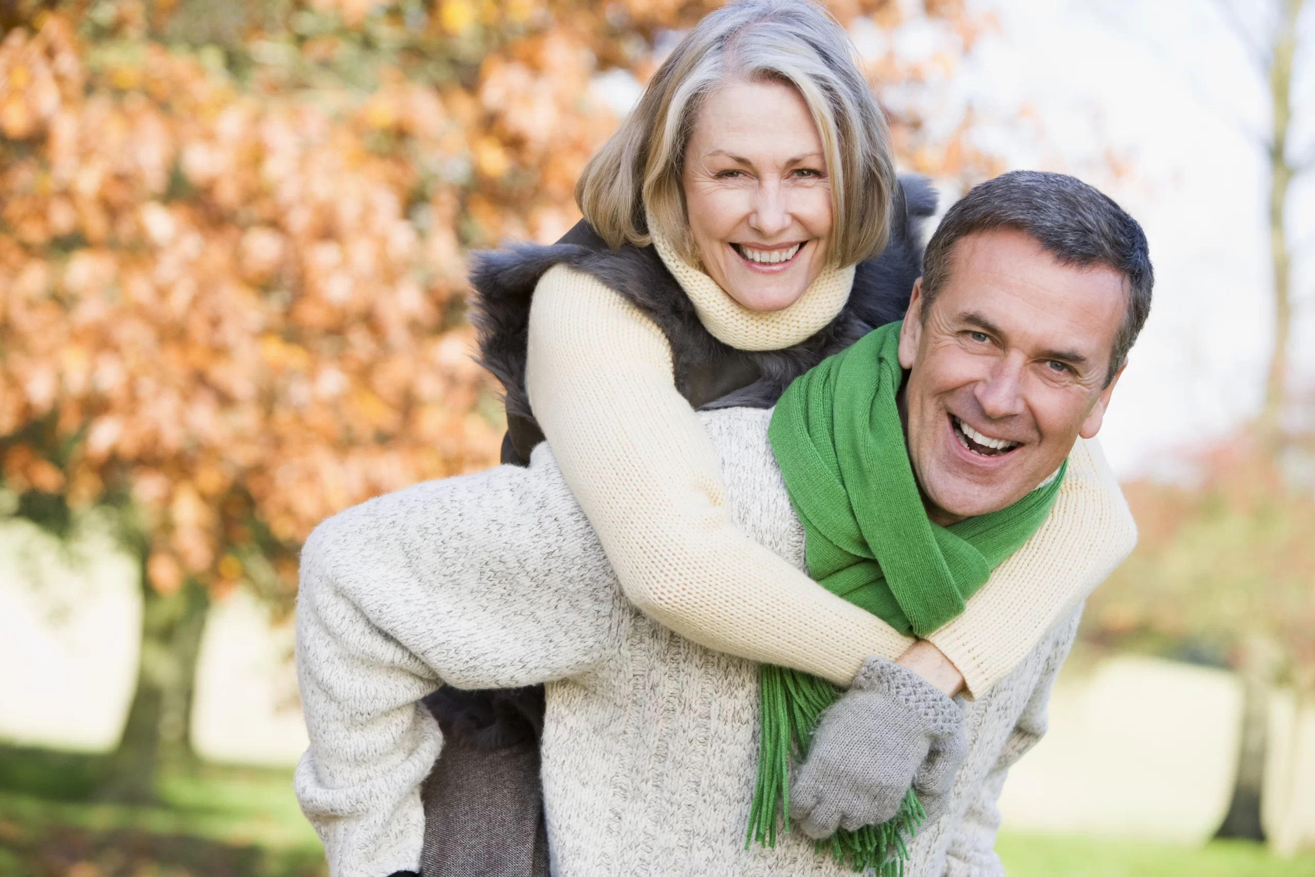 senior-man-giving-woman-piggyback-ride-through-autumn-woods